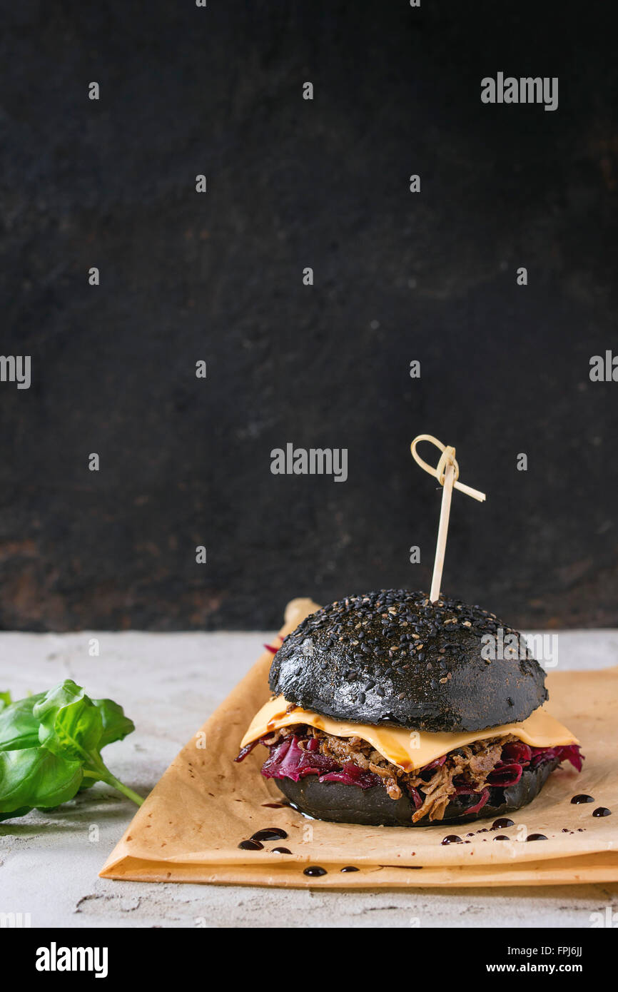 Burger de boeuf noir avec les ragoûts, fromage, choux rouge et sauce balsamique servi sur du papier sulfurisé avec le basilic sur plâtre gris Banque D'Images