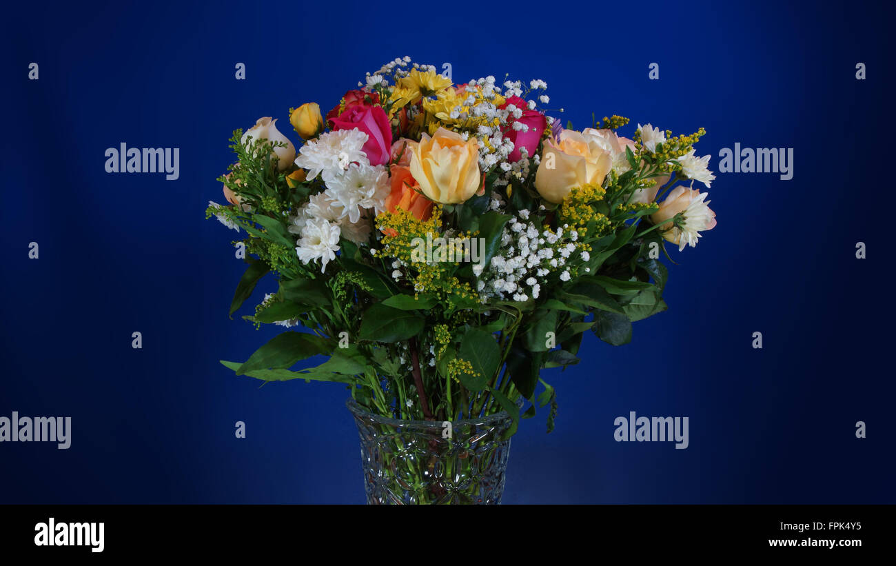 Bouquet de fleurs dans un vase de verre sur fond bleu foncé Banque D'Images