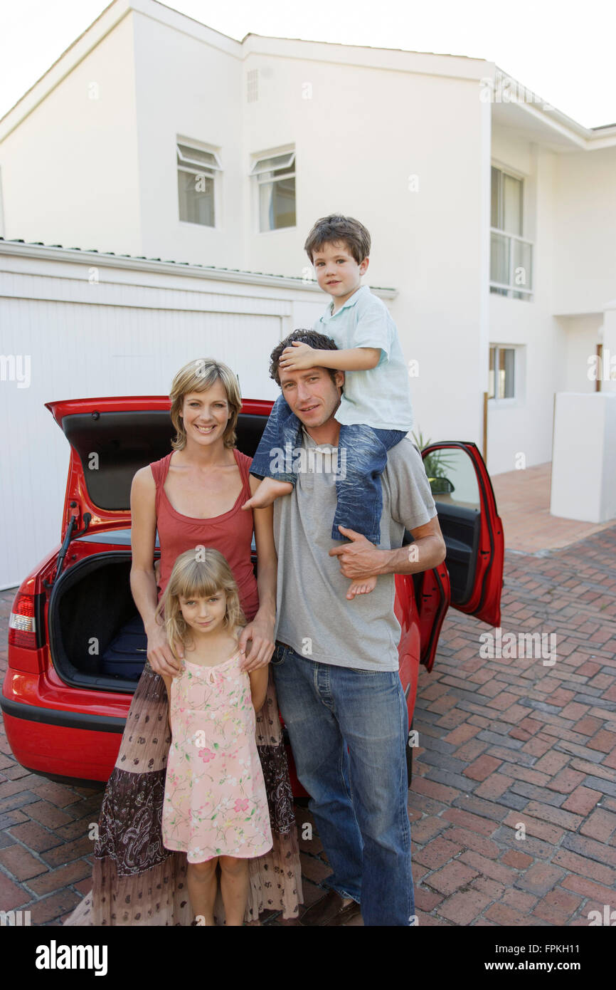 Famille avec 2 enfants debout devant de sa propre voiture et maison Banque D'Images