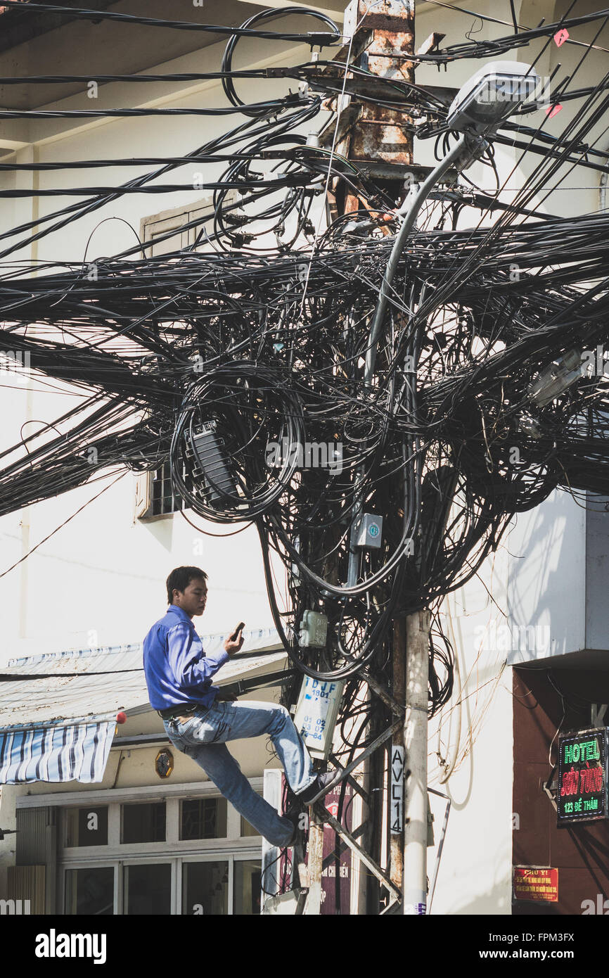 Saigon, Vietnam - le 20 janvier 2014 : Electrician fixing s'encombrer de câbles téléphone sur mât. Banque D'Images Saigon, Vietnam - le 20 janvier 2014 : Electrician fixing s'encombrer de câbles téléphone sur mât. Banque D'Images