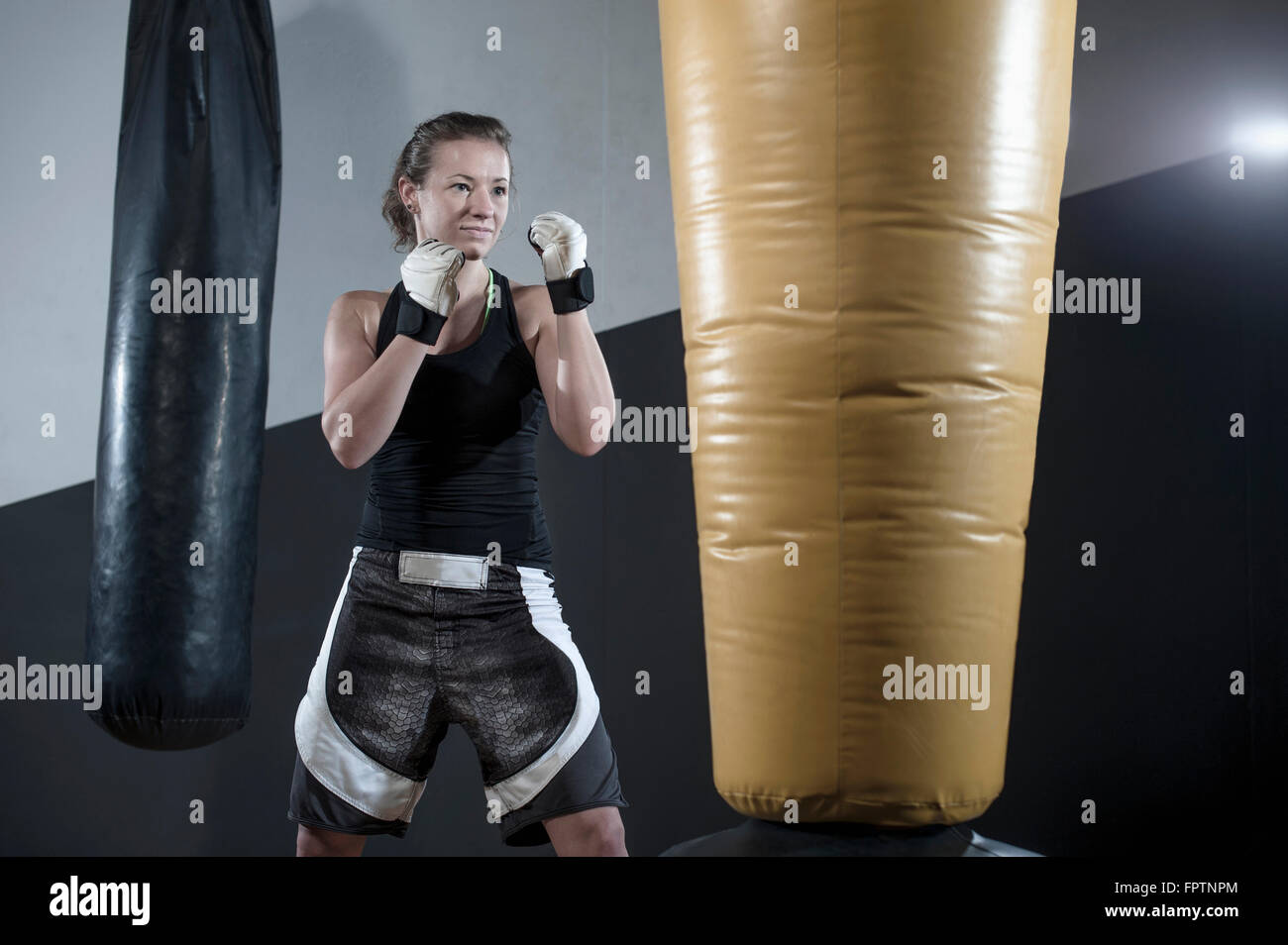 Jeune femme faisant la formation de force en enfonçant le sac dans la salle de sport, Bavière, Allemagne Banque D'Images