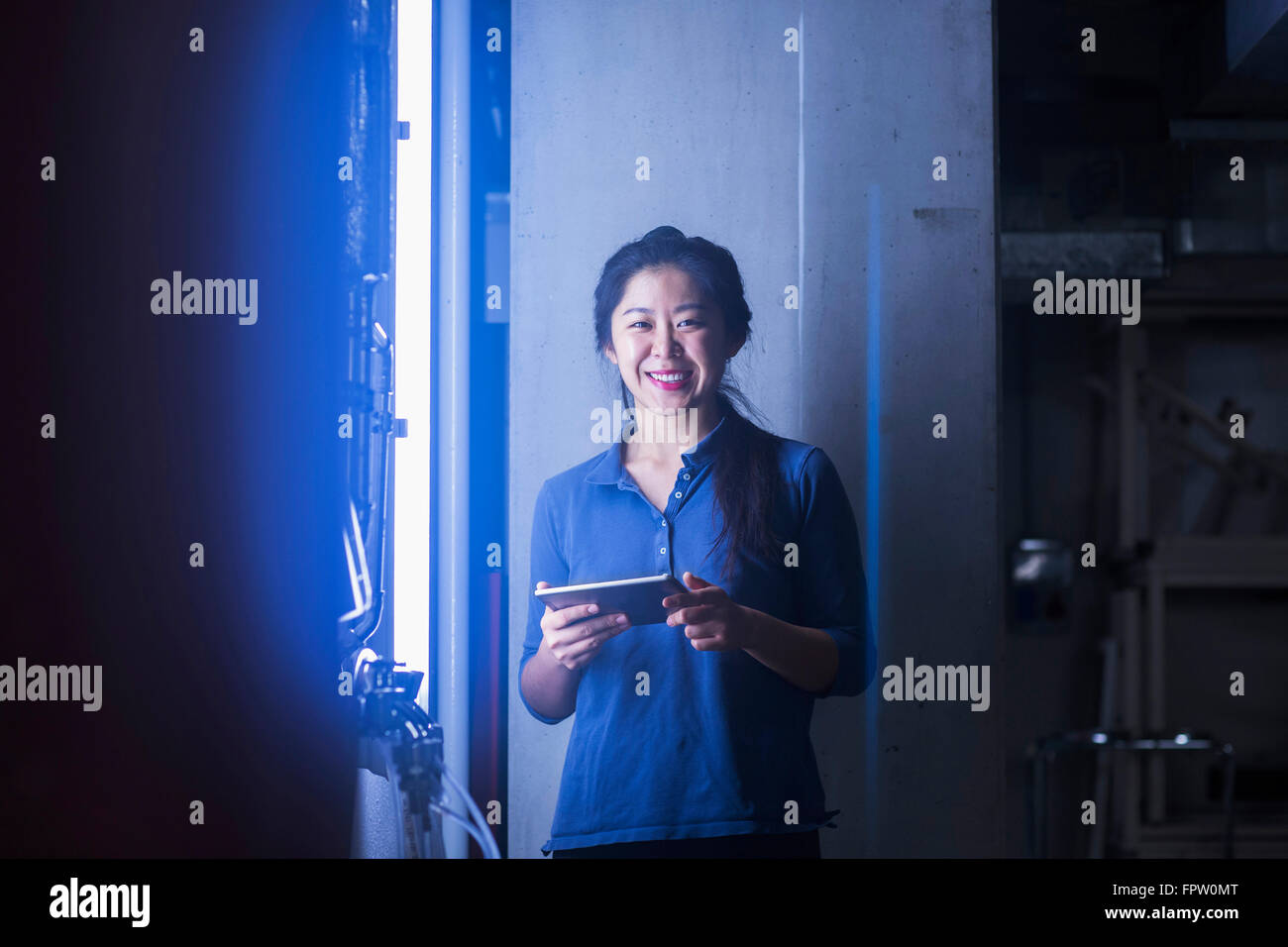 Jeune ingénieur femelle using digital tablet et souriant dans une installation industrielle, Freiburg im Breisgau, Bade-Wurtemberg, Allemagne Banque D'Images