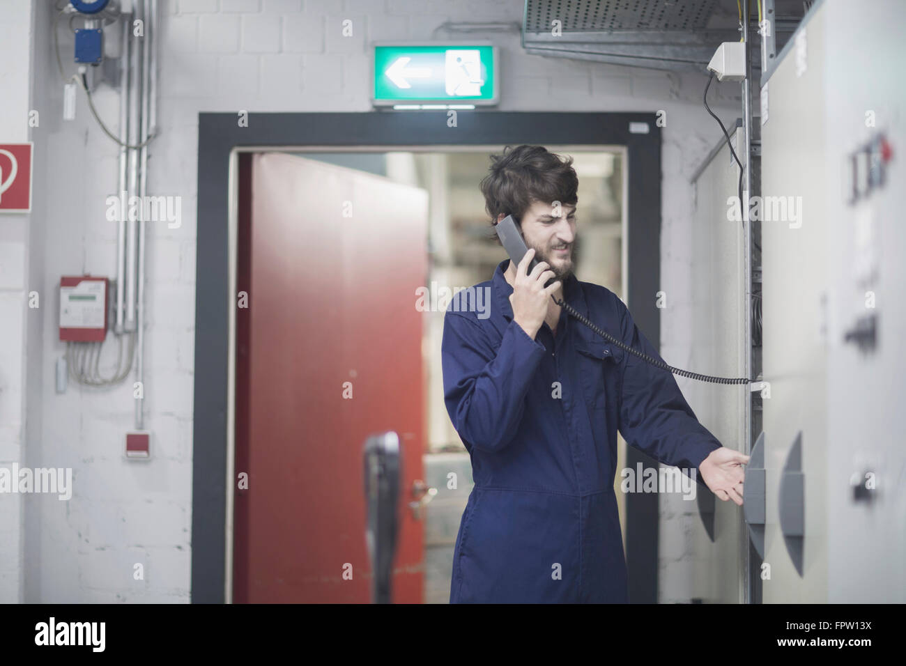 Ingénieur jeune mâle en conversation sur téléphone fixe dans une installation industrielle, Freiburg im Breisgau, Bade-Wurtemberg, Allemagne Banque D'Images