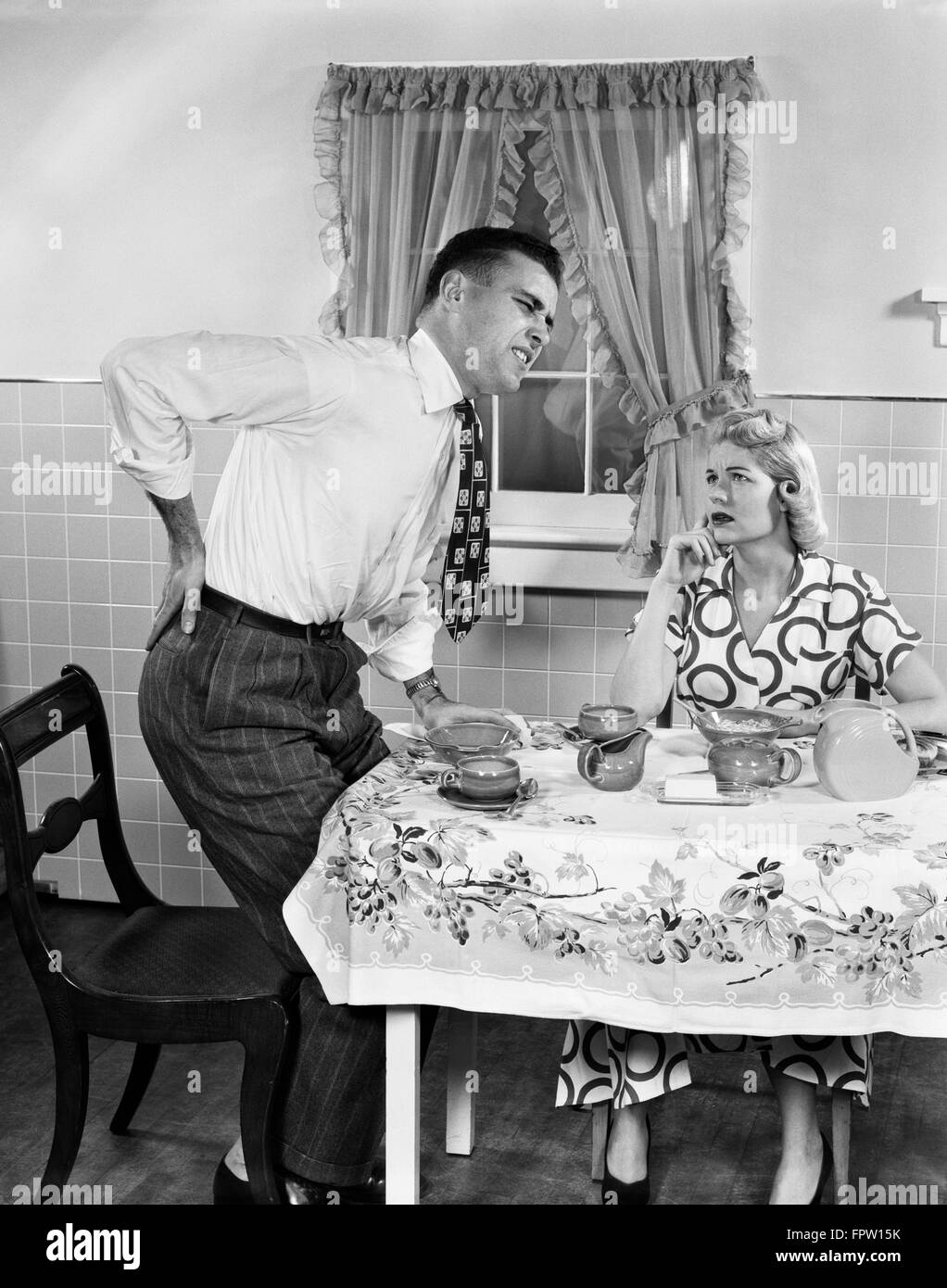 Années 50, Couple at Breakfast TABLE MAN WITH HAND ON HIP souffrant de maux de dos Banque D'Images