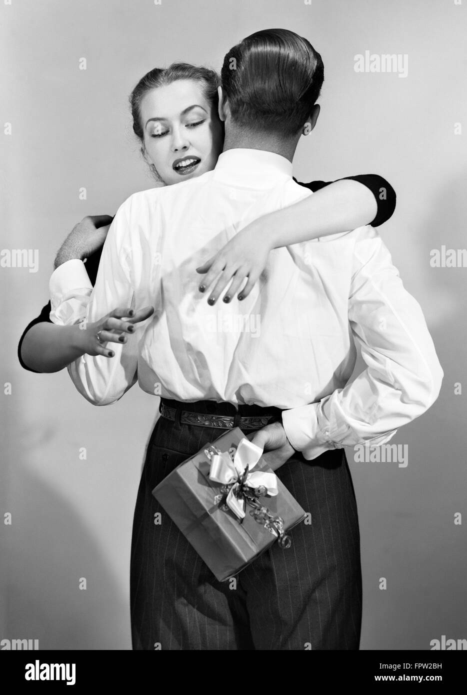 1950 FEMME COUPLE ATTEIGNANT ENVIRON DERRIÈRE LE DOS de l'homme pour s'emparer de présent Banque D'Images