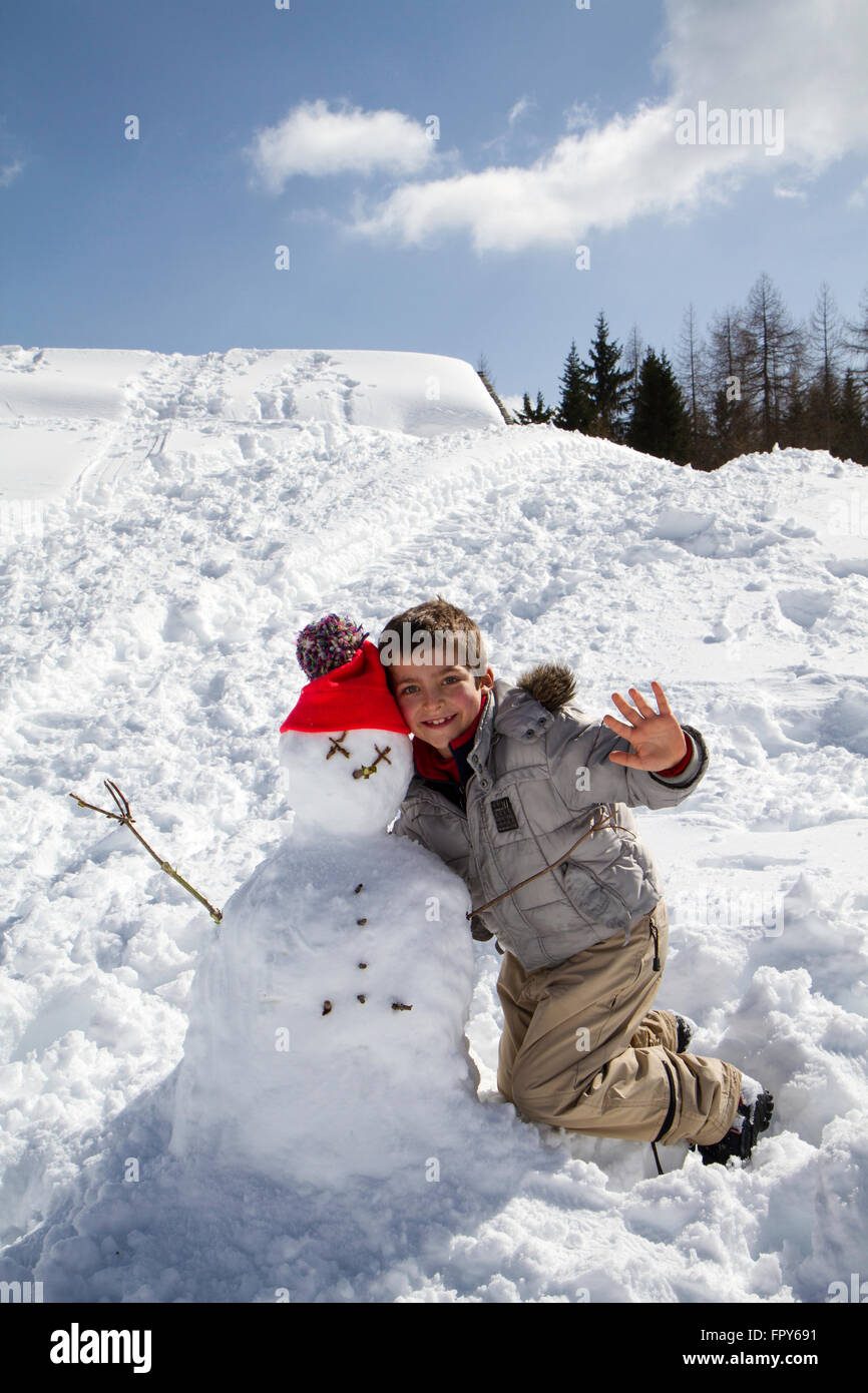 Enfant avec snowman avec chapeau en laine orange et bleu ciel Banque D'Images