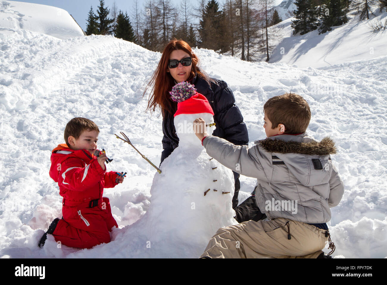 Deux frères et sa mère avec snowman avec chapeau en laine orange Banque D'Images