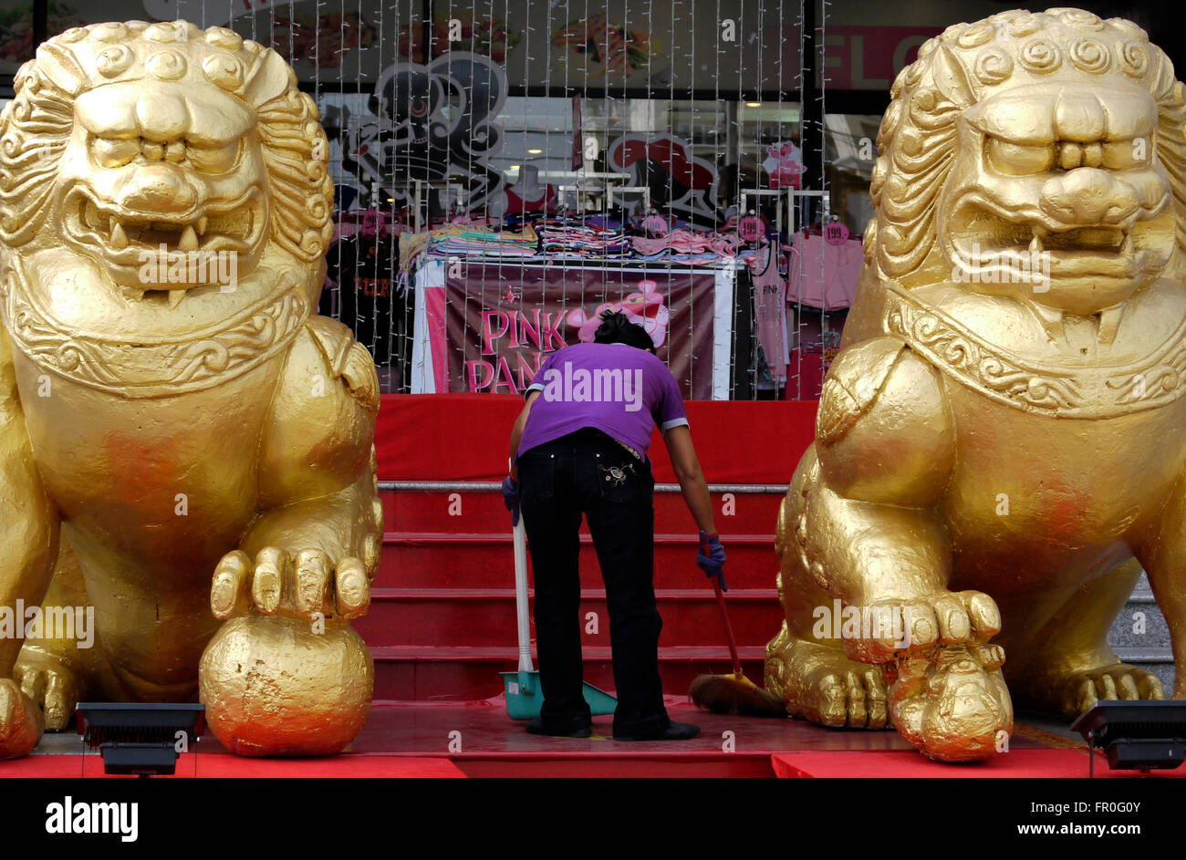 Cleaner au travail à l'extérieur d'un centre commercial à Pattaya en Thaïlande avant de célébrations spéciales avec une paire de "chien de Fo" (mi-chien mi-lion) Banque D'Images