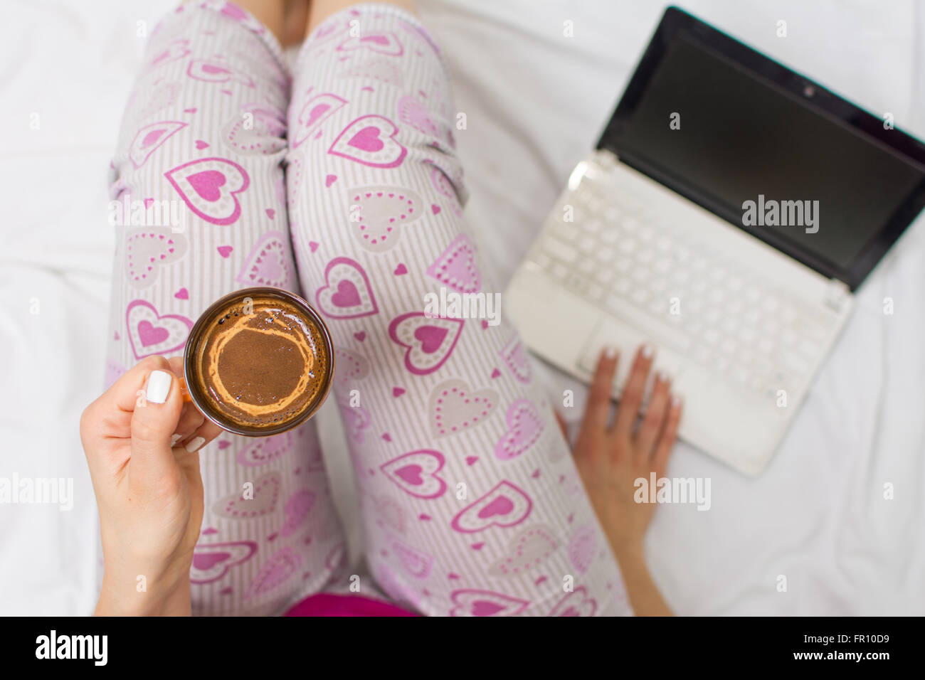 Femme ayant une tasse de café au lit avec un ordinateur portable Banque D'Images