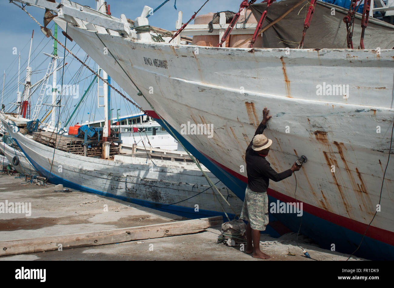 Un homme sands la coque d'un bateau avant peinture. Le Port de Paotere bien connu comme un vieux port. Banque D'Images