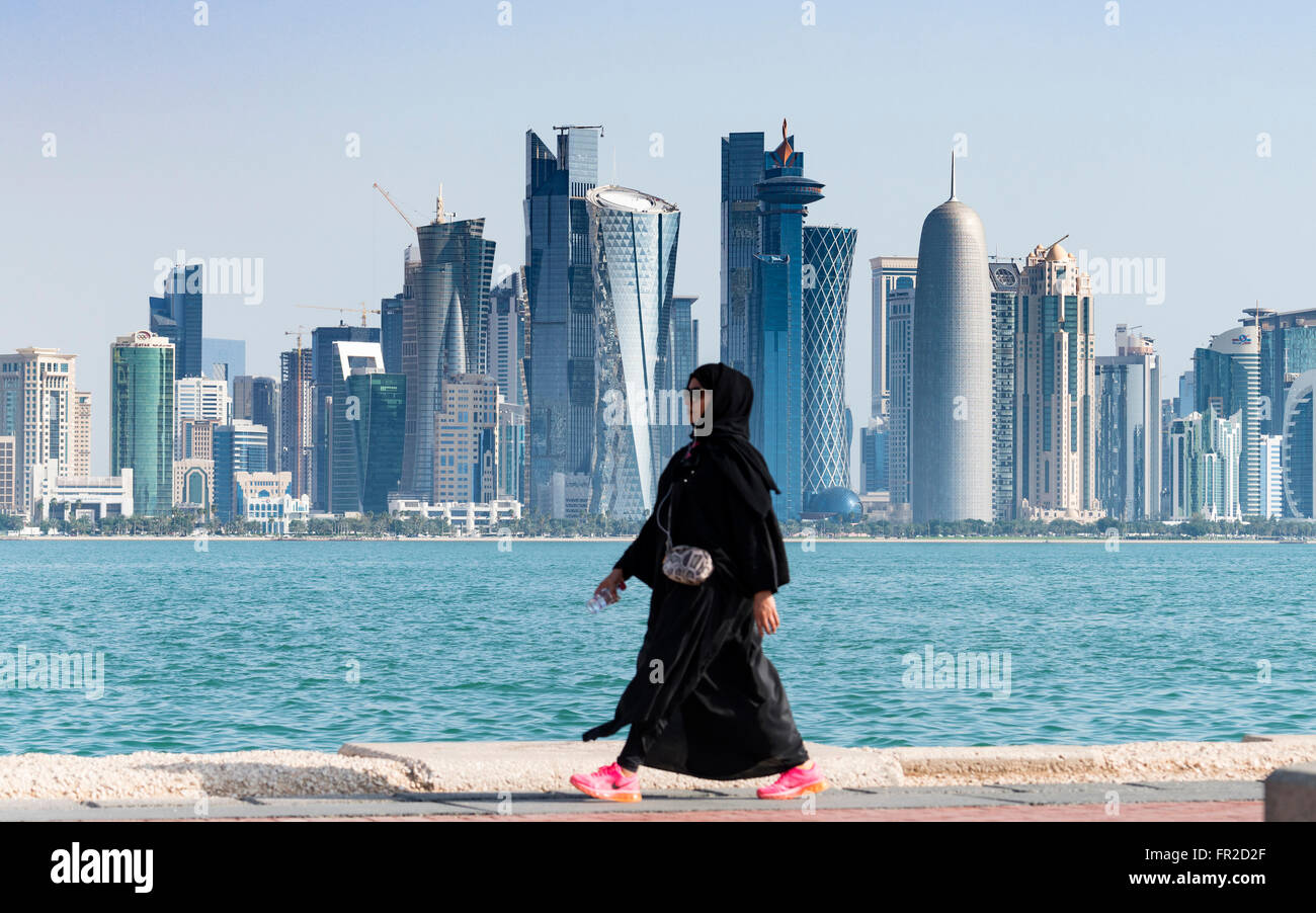 Femme qatarie en abaya à marcher le long de la Corniche du front de mer vers les tours de bureaux modernes à West Bay, quartier financier et d'affaires à Doha Qatar Banque D'Images