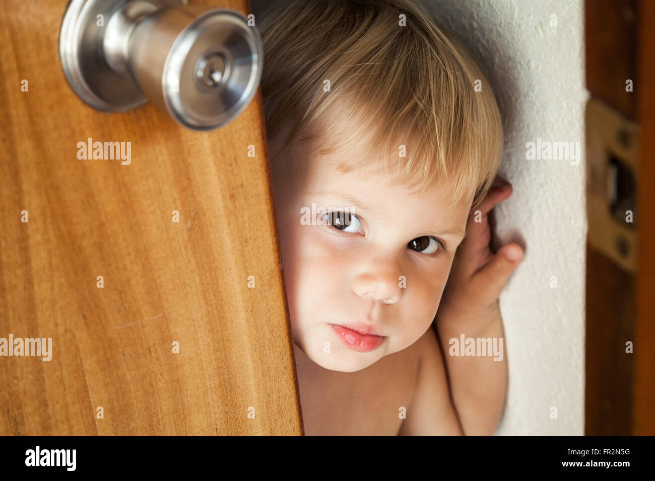 Petit blond bébé fille ouvre la porte et se tourne vers l'extérieur Banque D'Images