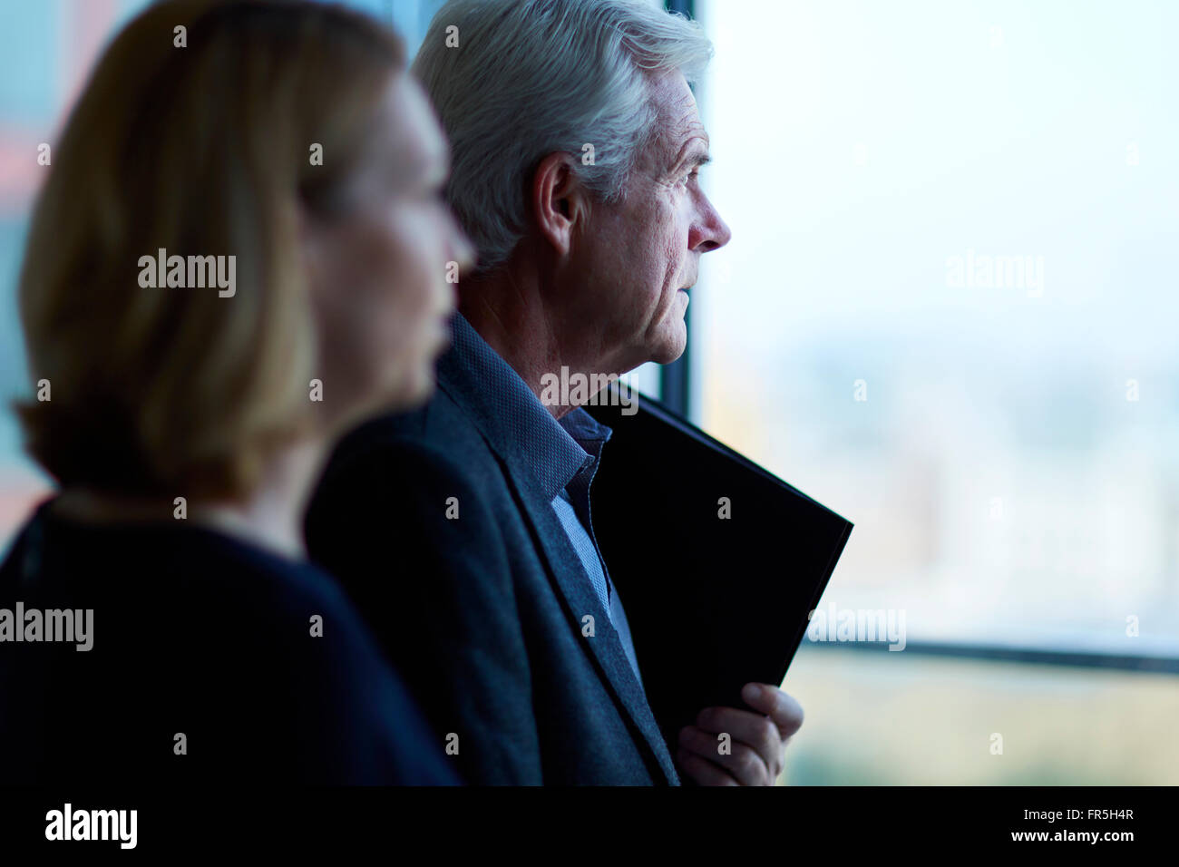 Pensive businessman and businesswoman looking through window Banque D'Images