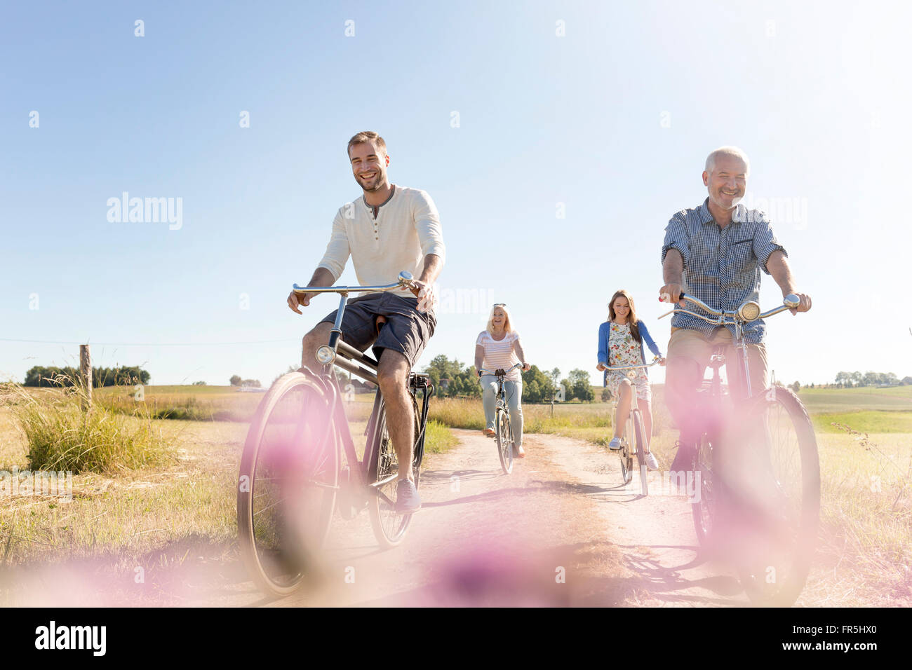 Family riding bicycles sur chemin de terre rurale ensoleillée Banque D'Images