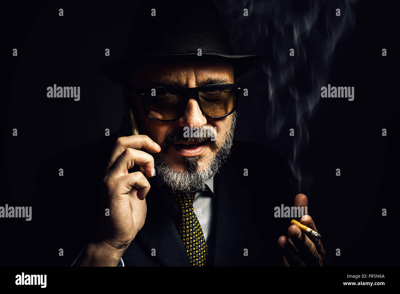 Portrait d'un homme plus âgé, portant un chapeau et veste classique, fumer un cigare et de parler par téléphone. Banque D'Images