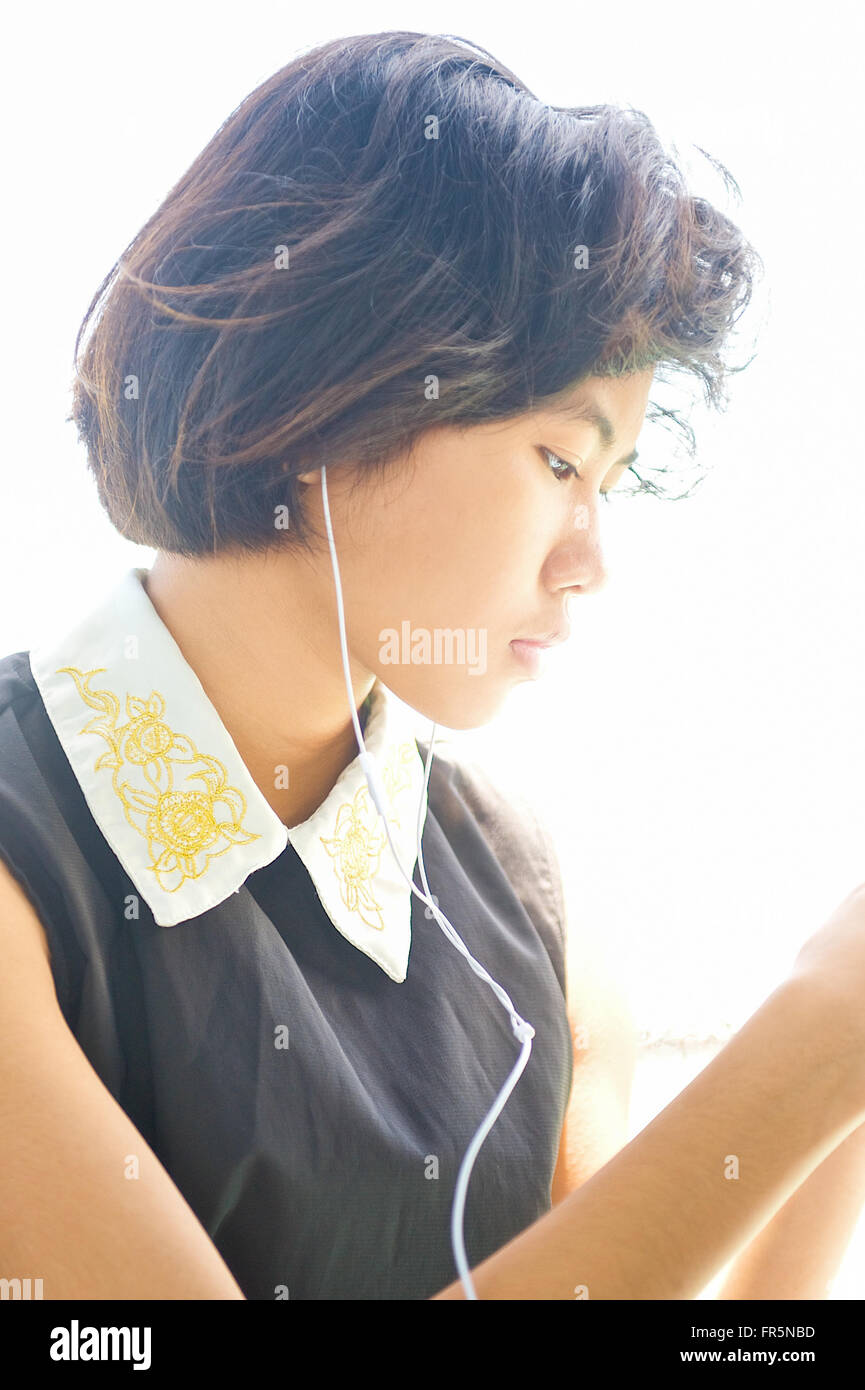 Une belle jeune adolescente thaïlandaise est assis à écouter sa musique sur son téléphone avec ses écouteurs à Bangkok en Thaïlande, Asie Banque D'Images