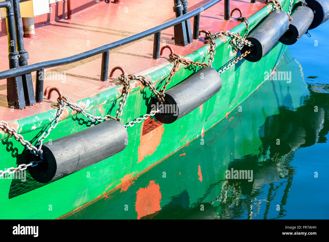 Une quille de bateau vert avec butées en caoutchouc noir dans de l'eau réfléchissante. Banque D'Images