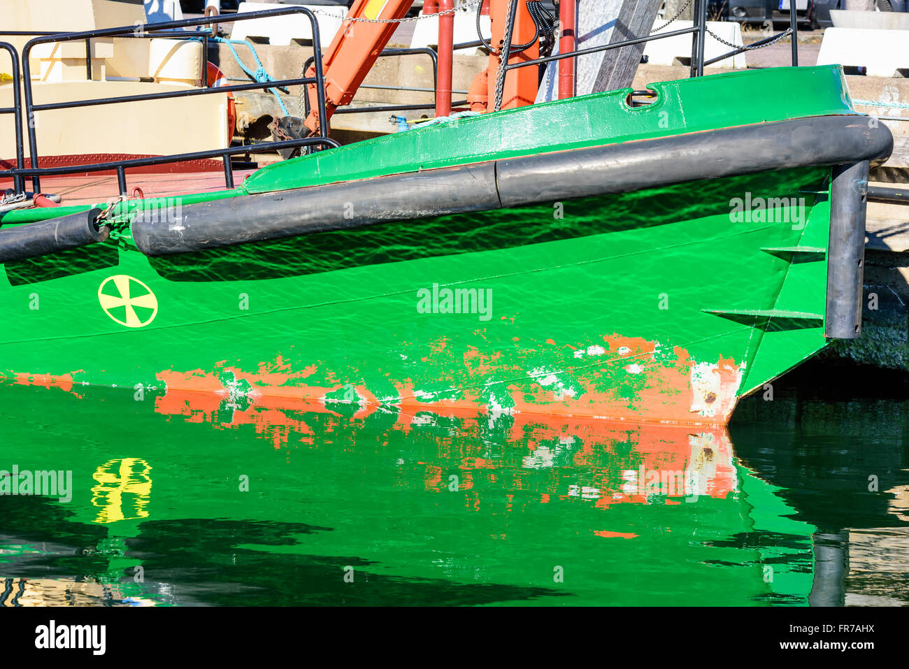 Une quille de bateau vert avec butées en caoutchouc noir dans de l'eau réfléchissante. Banque D'Images