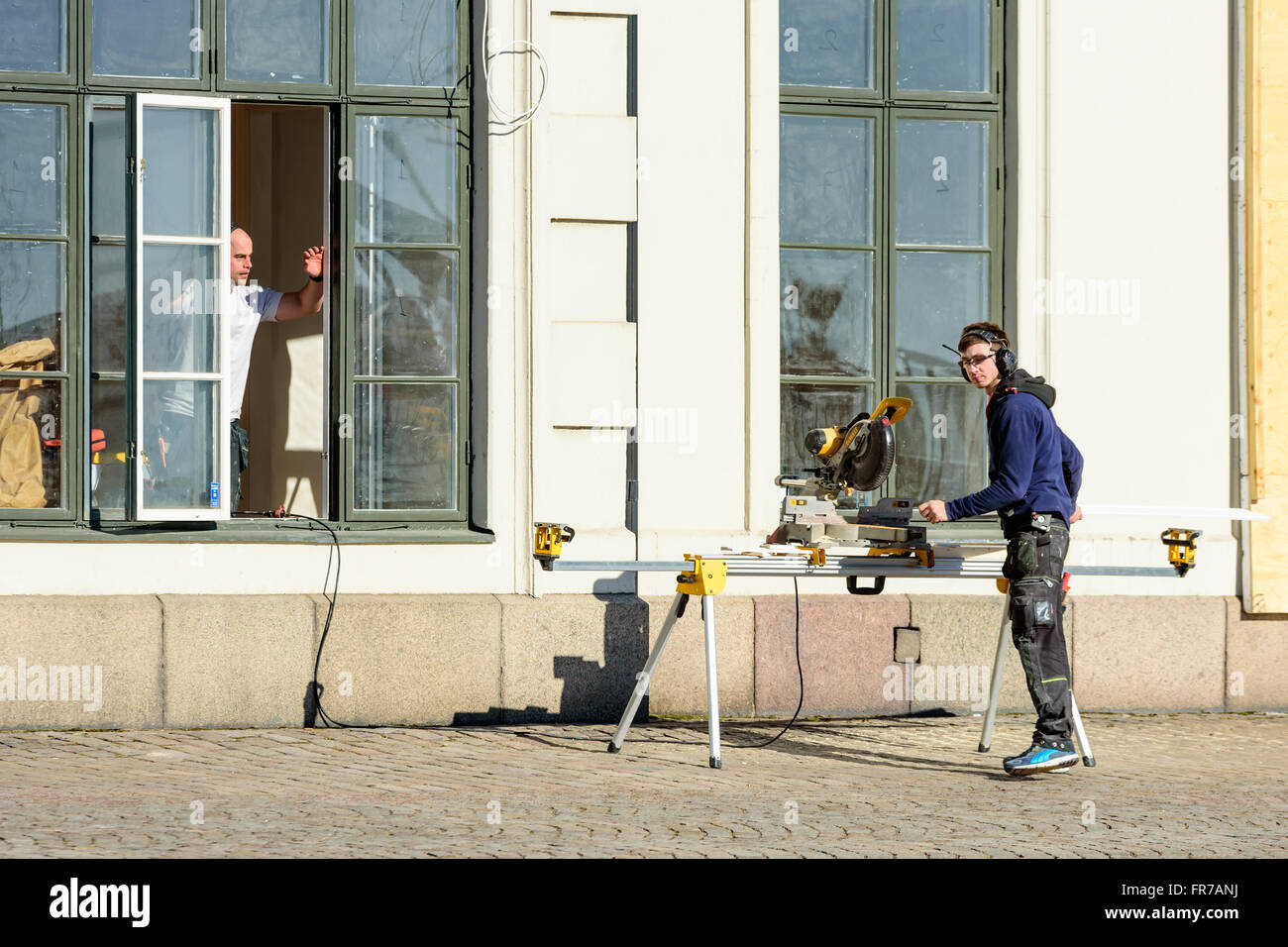Kalmar, Suède - Mars 17, 2016 : un jeune adulte à l'extérieur de la fenêtre Gérer une scie à onglets et remettre les planches sciées t Banque D'Images