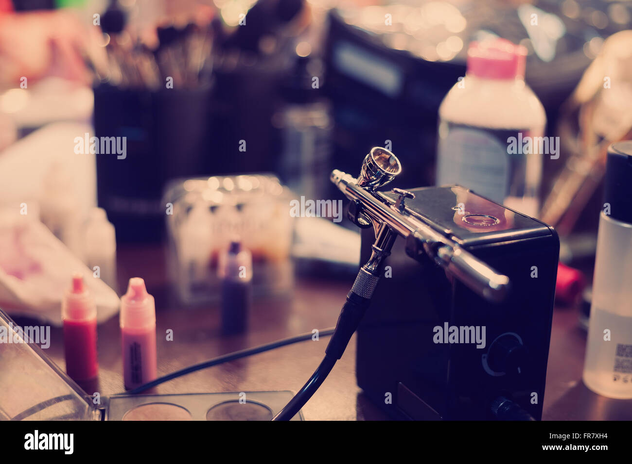 Airbrusher pour maquillage professionnel dans un studio debout sur une table de visagiste. Les cosmétiques et les pinceaux sur l'arrière-plan. Couleurs hipster moderne Banque D'Images