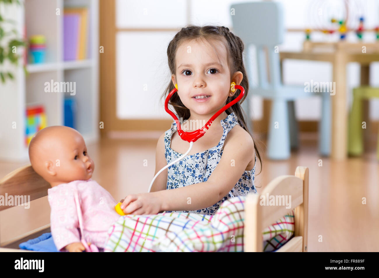 Kid toddler playing rôle médecin examinant sa poupée à l'aide de jeu de stéthoscope de jeux à la maison, à l'école ou au jardin d'enfants Banque D'Images