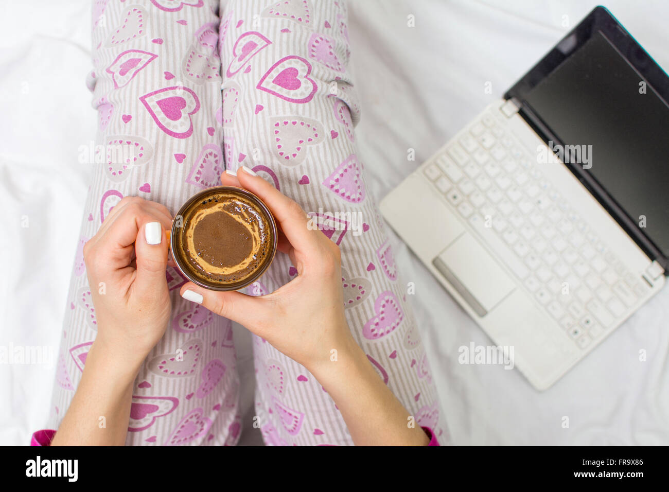 Femme ayant une tasse de café au lit avec un ordinateur portable Banque D'Images