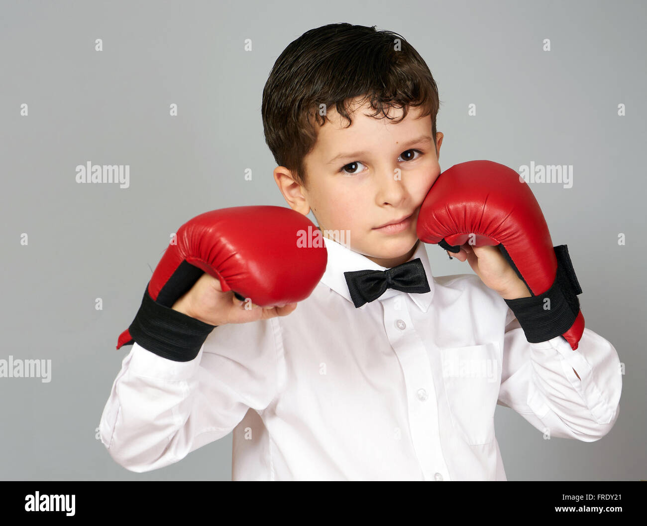 Cinq ans garçon en chemise blanche et nœud papillon avec boxingcarate sur les mains des gants Banque D'Images