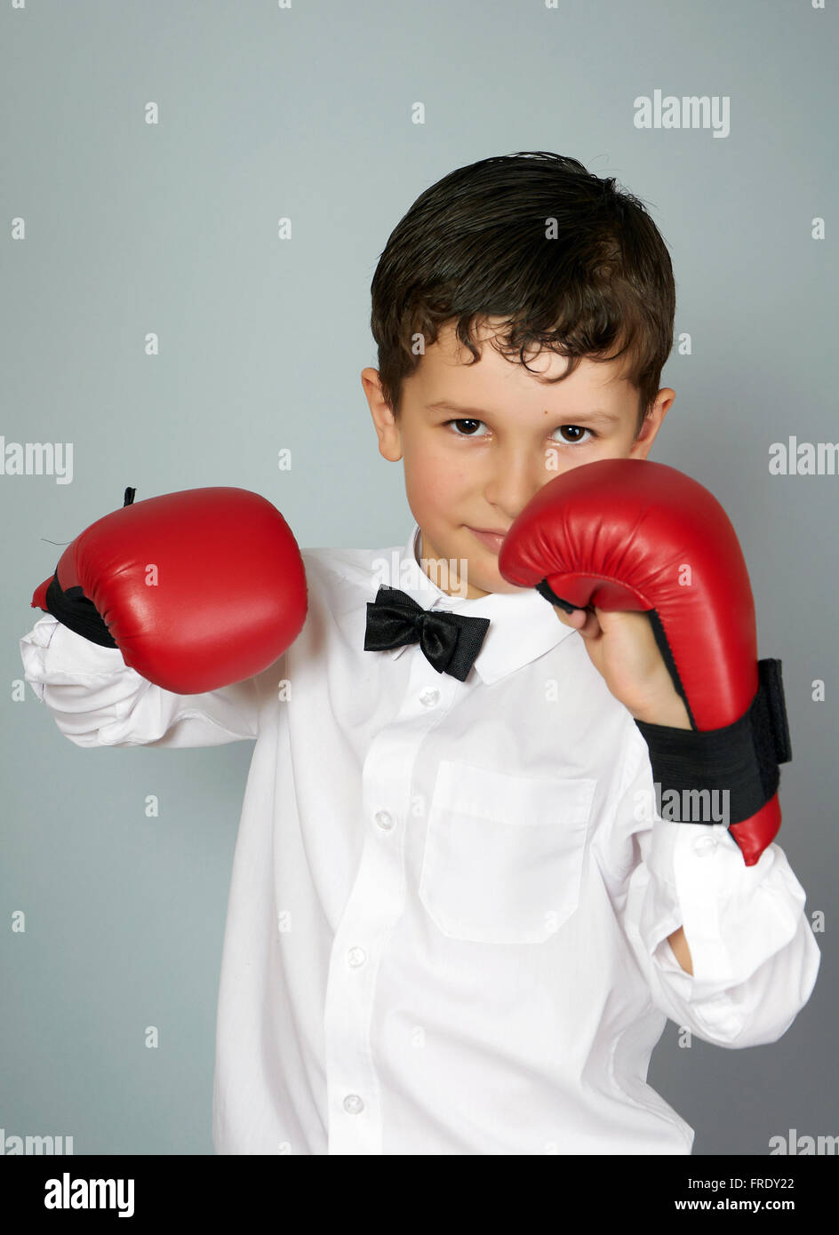 Cinq ans garçon en chemise blanche et nœud papillon avec boxingcarate sur les mains des gants Banque D'Images