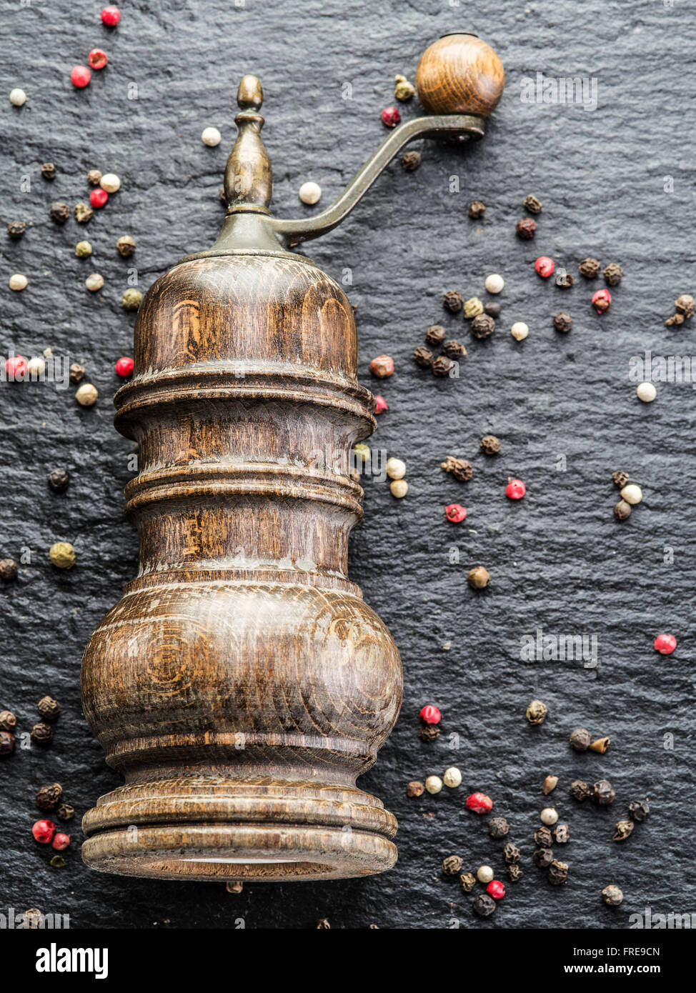 Poivre en grains colorés et vieux moulin à poivre sur le fond noir. Banque D'Images