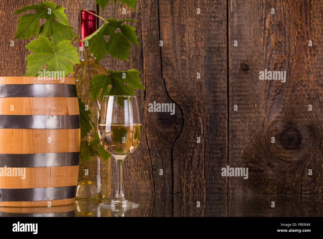 Verre de vin en bouteille blanche fourreau derrière grapeleaves en bois foncé et contexte Banque D'Images
