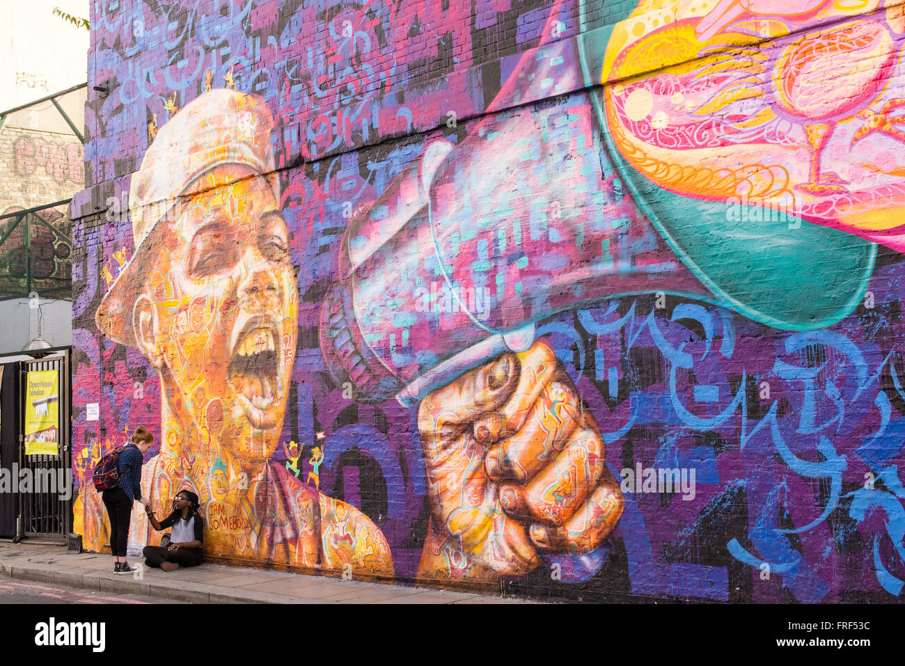 Trois adolescentes debout devant un mur avec une grande zone d'écriture graffiti représentant un garçon crier avec un haut-parleur. Banque D'Images