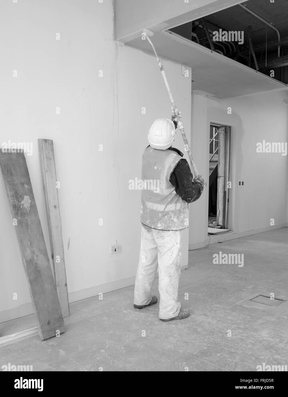 Décorateur commercial au travail en peinture d'un haut plafond avec un rouleau à peindre Banque D'Images
