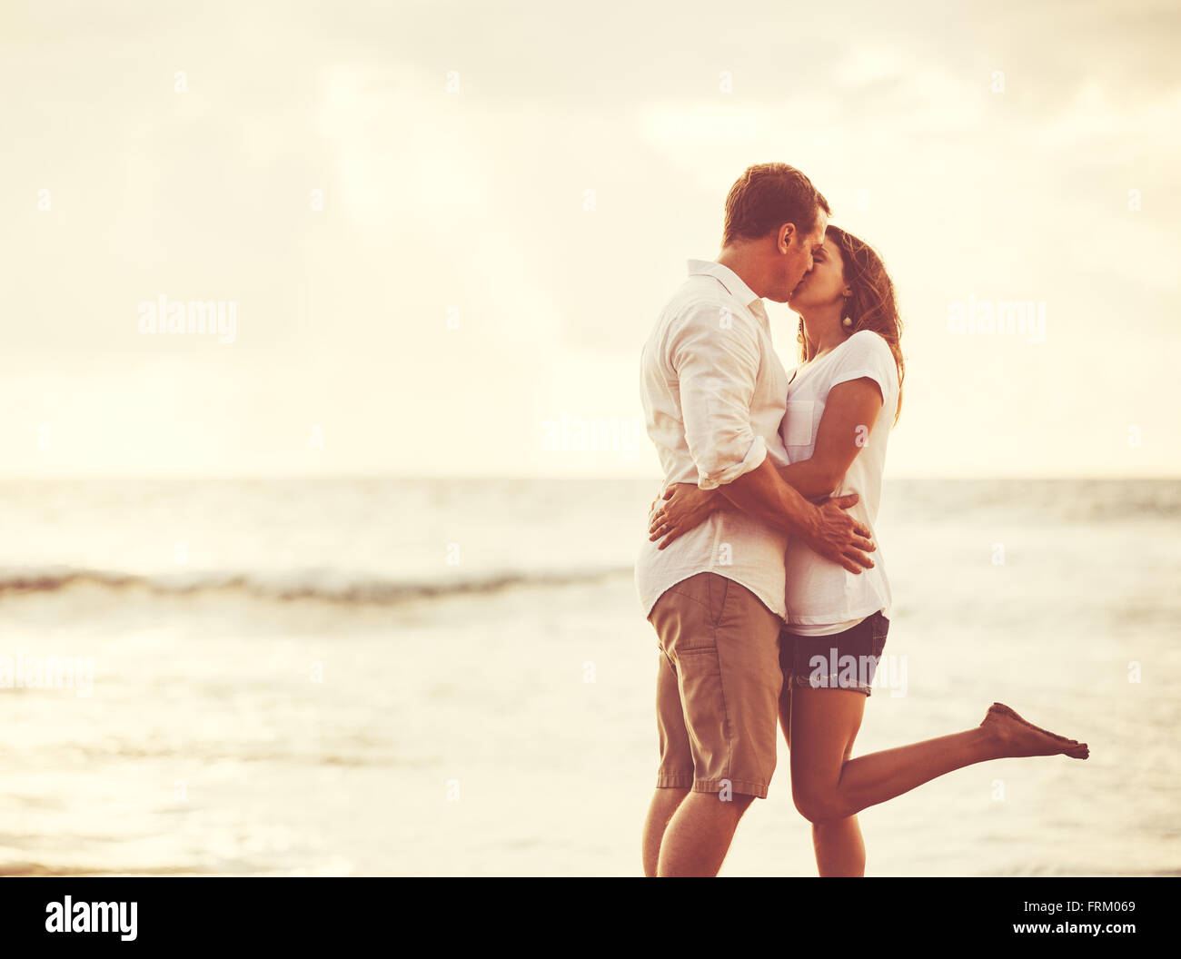 Heureux couple romantique sur la plage au coucher du soleil. Les jeunes amoureux en vacances. Banque D'Images