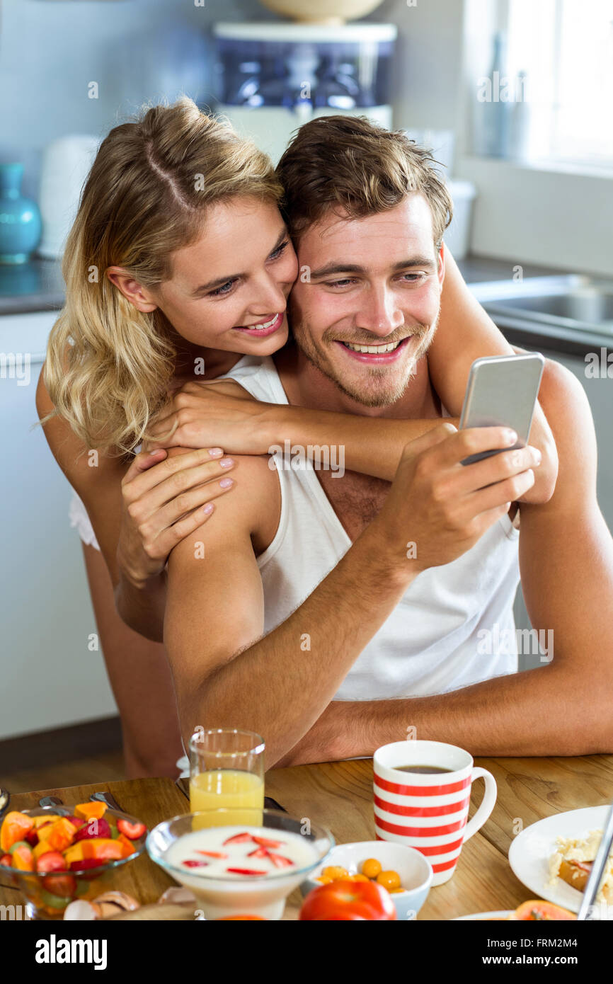 Woman embracing man using mobile phone at home Banque D'Images