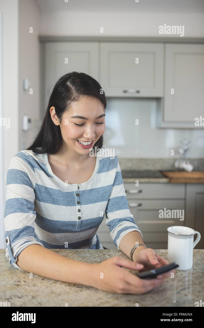 Femme heureuse de la saisie d'un message texte sur son téléphone portable dans la cuisine Banque D'Images