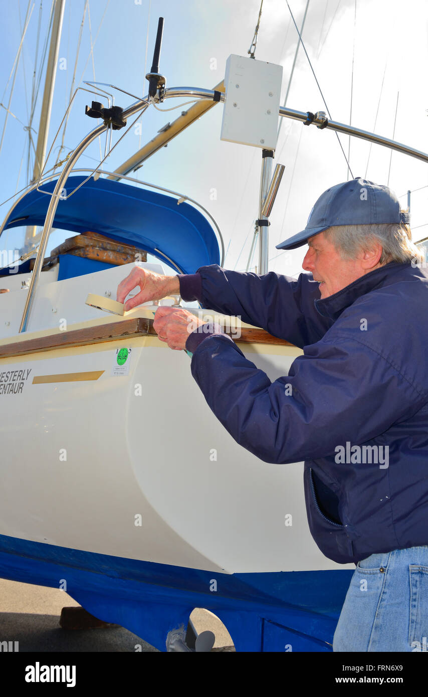 Propriétaire de bateau à l'aide du ruban de masquage en préparation à la frotter en bois vernis sur ses virures Centaur Ouest location Banque D'Images