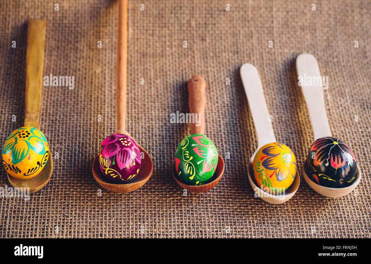 Les oeufs de Pâques colorés peints magnifiques couchés sur des cuillères en bois sur un fond de toile de jute Banque D'Images