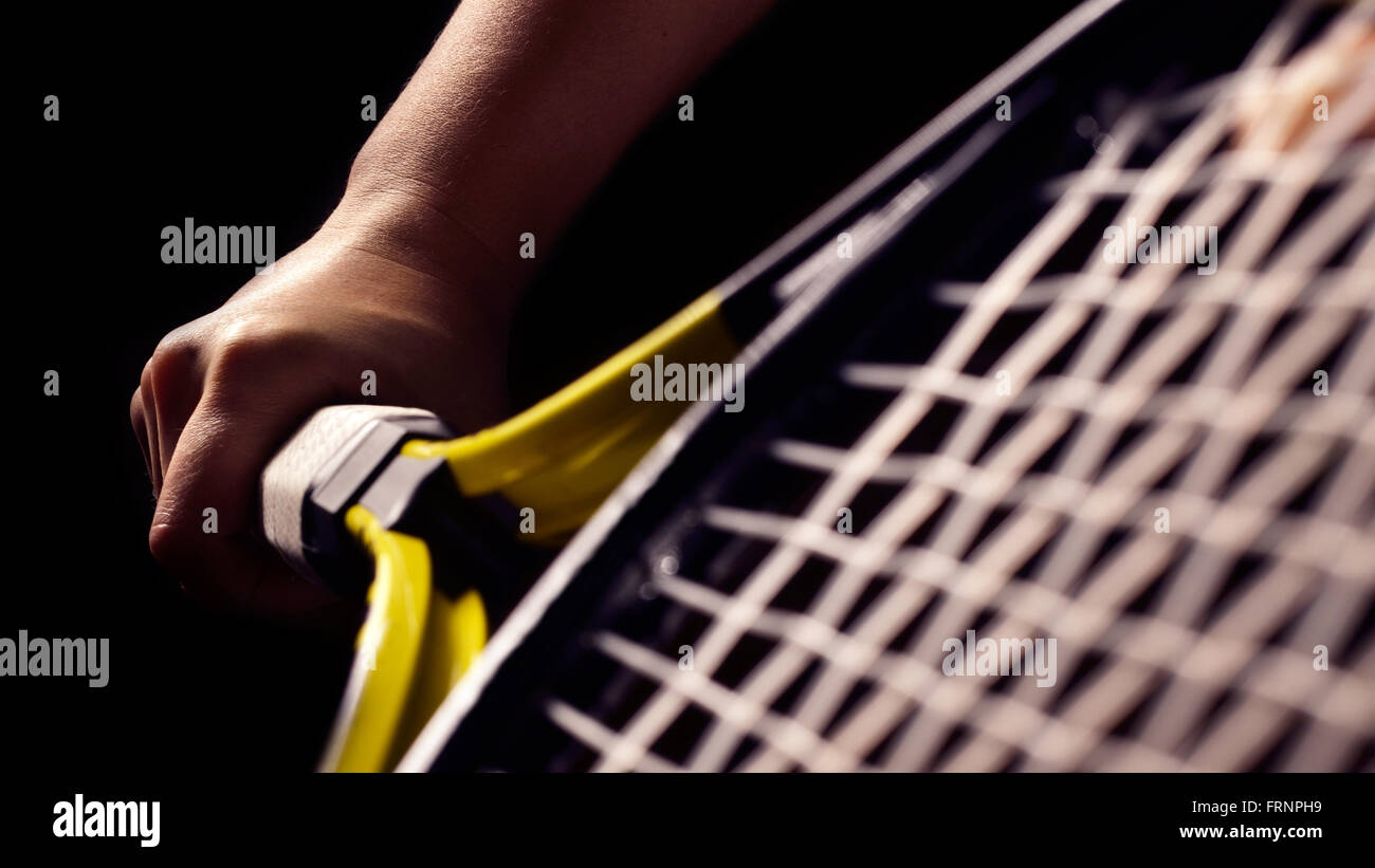 Main sur l'adhérence et balançant une raquette de tennis. Isolé sur fond noir. Banque D'Images