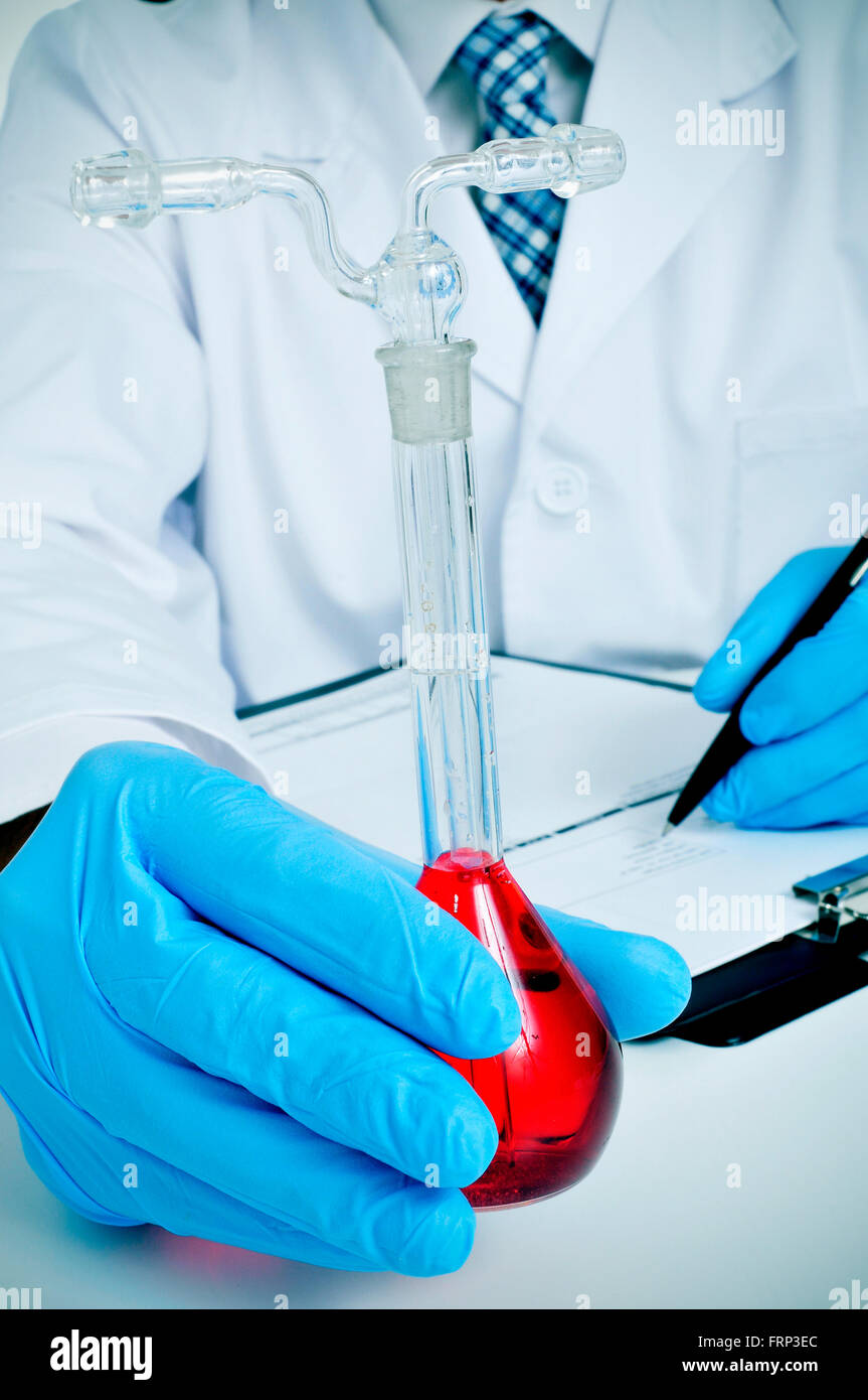 Libre d'un jeune homme de race blanche en robe blanche avec une fiole jaugée avec un liquide rouge dans sa main dans un laboratoire Banque D'Images