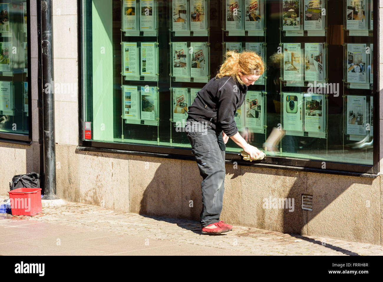 Kalmar, Suède - le 17 mars 2016 : personne de sexe féminin le nettoyage windows sur un magasin. Elle utilise un chiffon et a son seau d'eau rouge être Banque D'Images