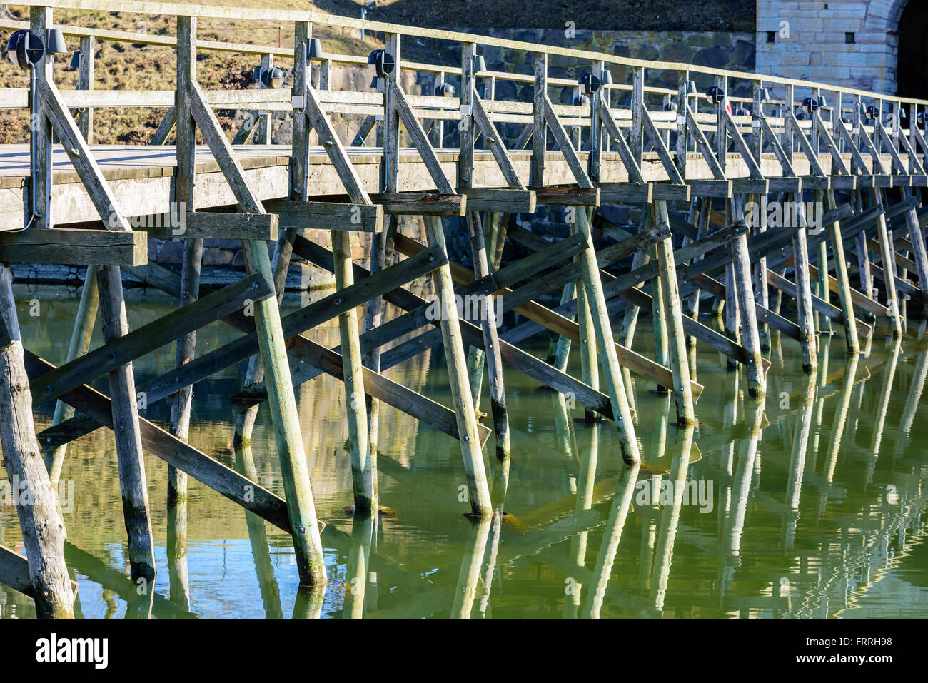 Un vieux pont en bois sur l'eau, menant à un mur en pierre partiellement visible à droite. Ce pont mène à l'ouest de c Banque D'Images