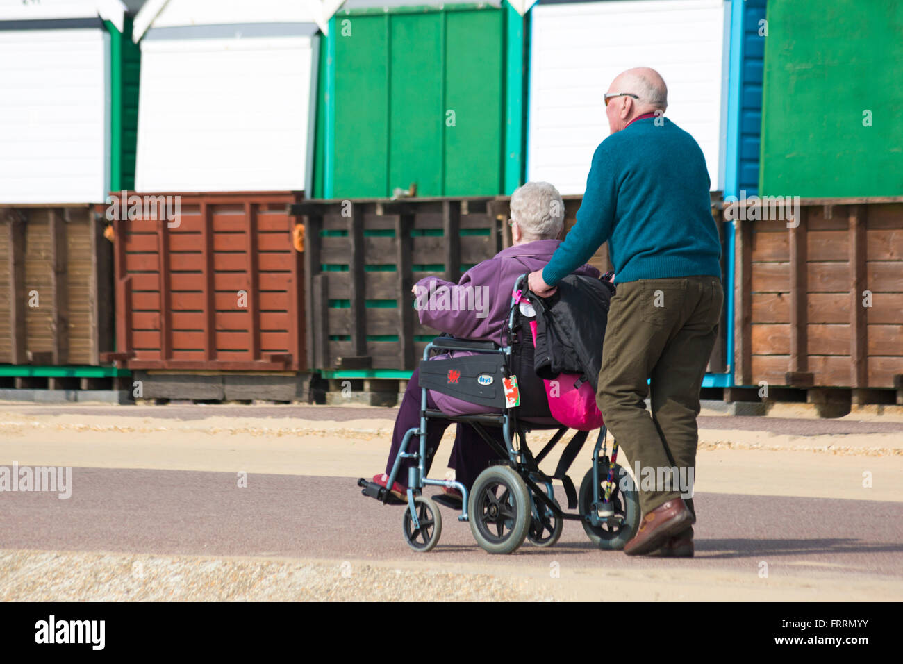 Man pushing woman in wheelchair promenade le long cours des cabanes de plage au milieu Chine, Bournemouth en Mars Banque D'Images