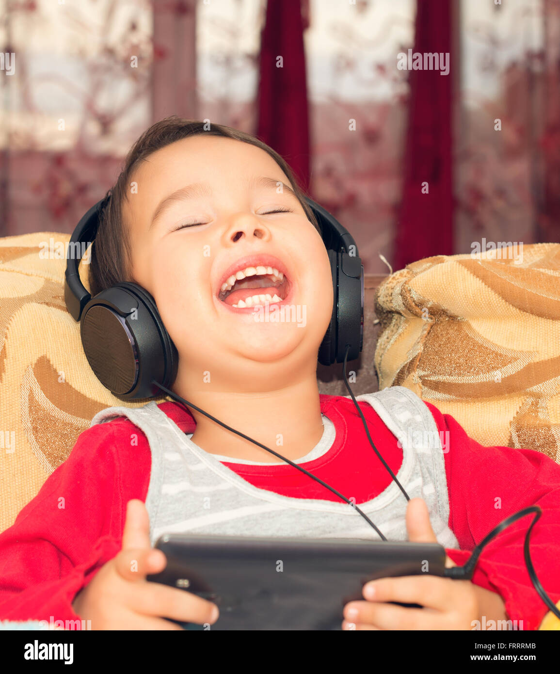 Petite fille sur le canapé avec les écouteurs et la musique d'du smartphone Banque D'Images