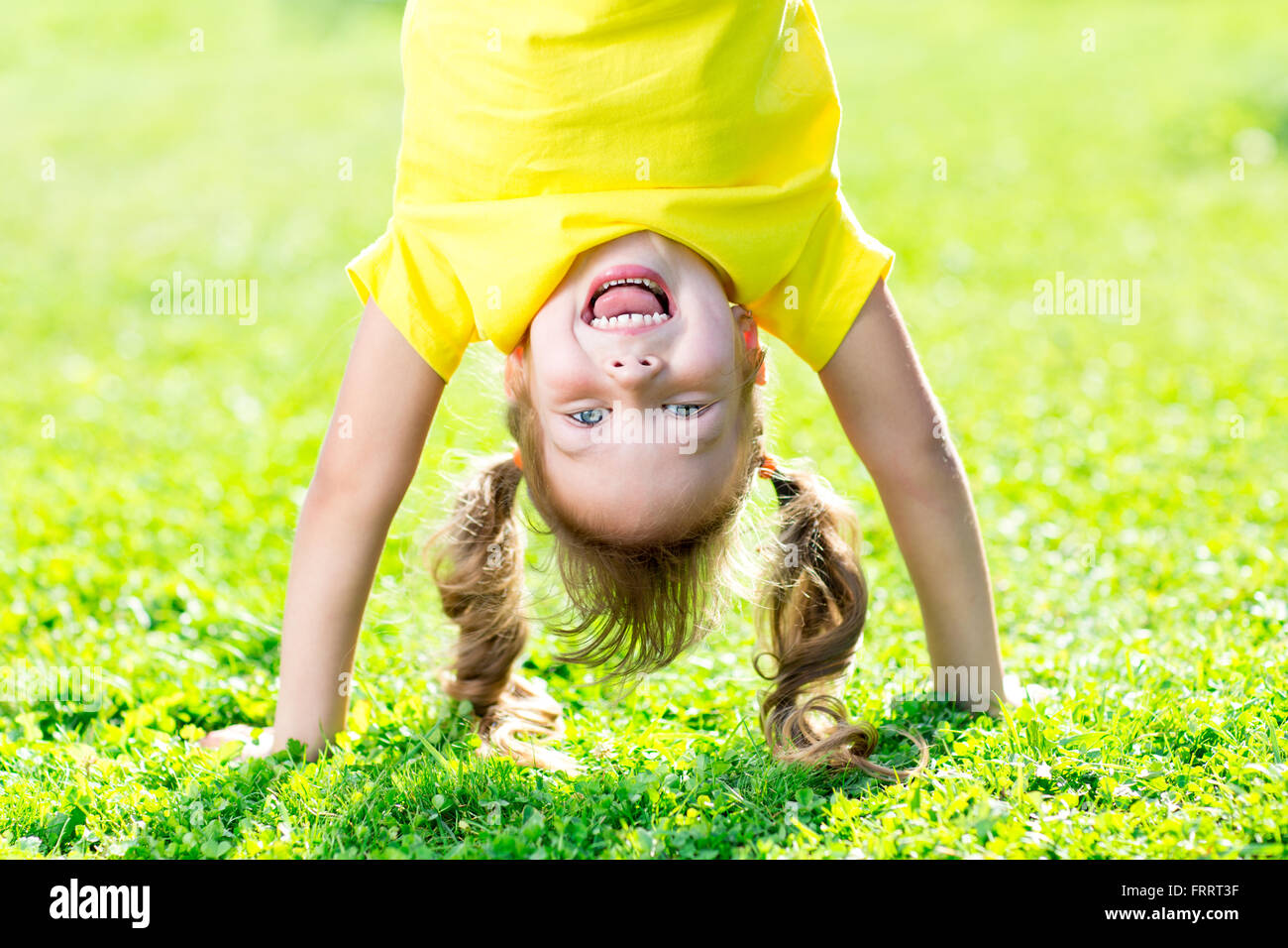 Portraits d'enfants heureux de jouer à l'envers l'extérieur en été, debout sur les mains sur l'herbe Banque D'Images