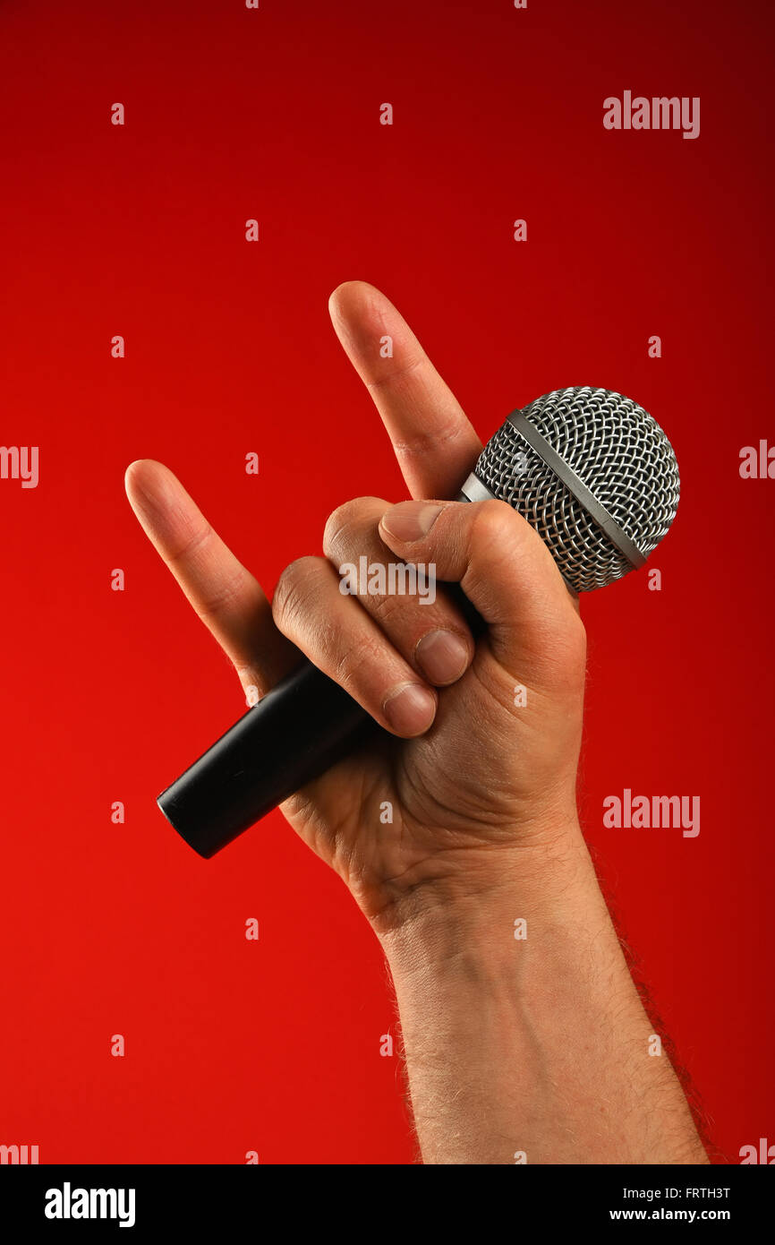 Man hand holding microphone vocal avec des cornes de diable geste rock metal sign sur fond rouge, front view Banque D'Images