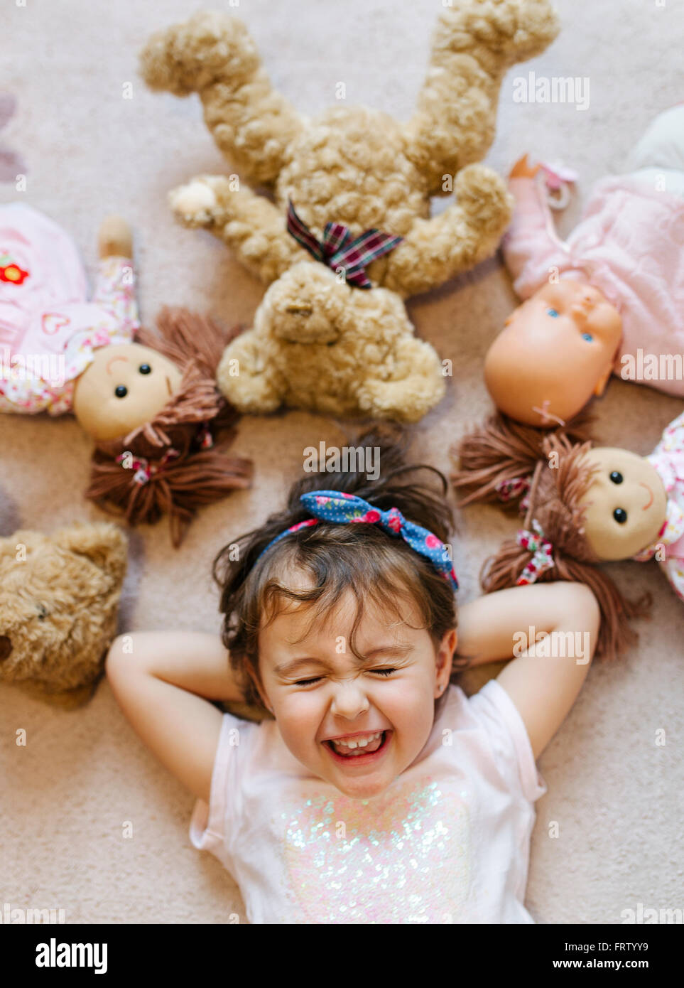 Portrait of laughing petite fille gisant sur le sol avec des collants et des poupées autour d'elle Banque D'Images