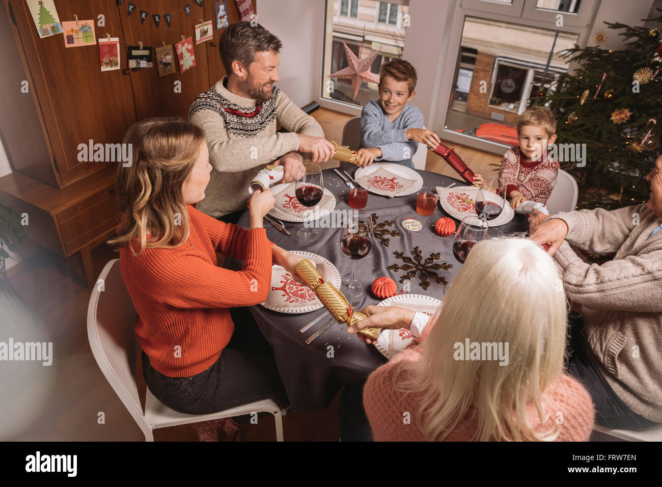 Une famille heureuse de trois générations en tirant en extrémités de cloches de Noël avant le dîner Banque D'Images