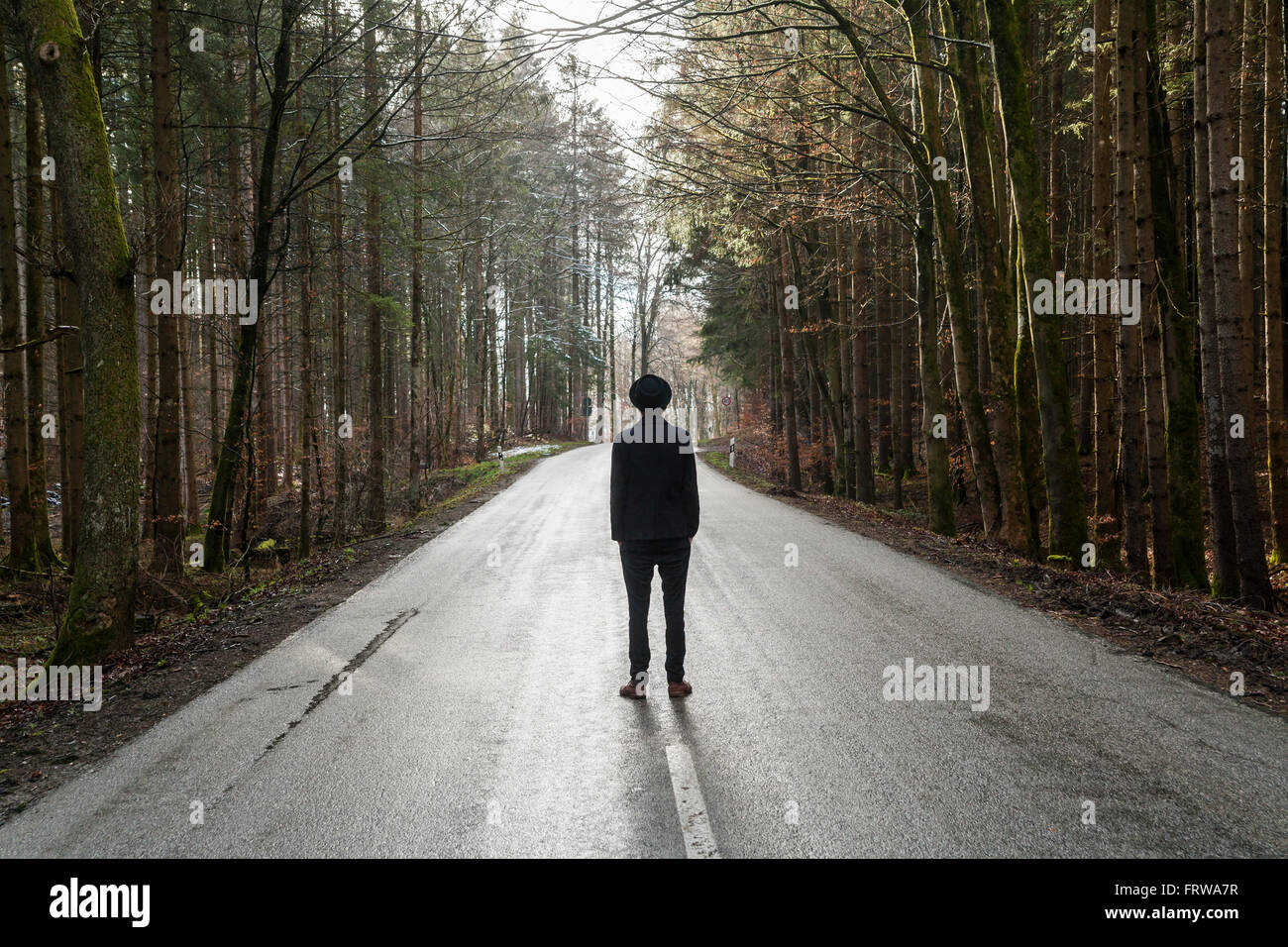 Allemagne, vue arrière de jeune homme habillé en noir debout sur empty country road Banque D'Images