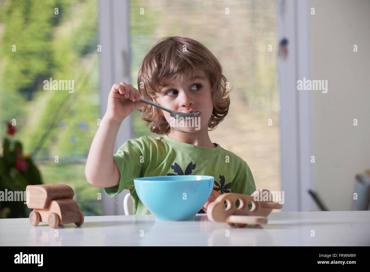 Cute little boy de manger son repas tout en jouant avec des jouets Banque D'Images