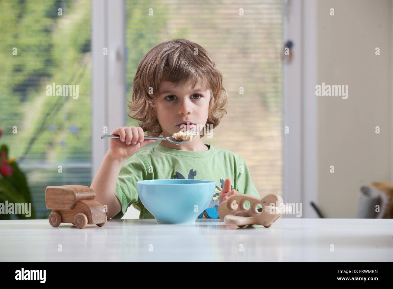 Cute little boy de manger son repas tout en jouant avec des jouets Banque D'Images